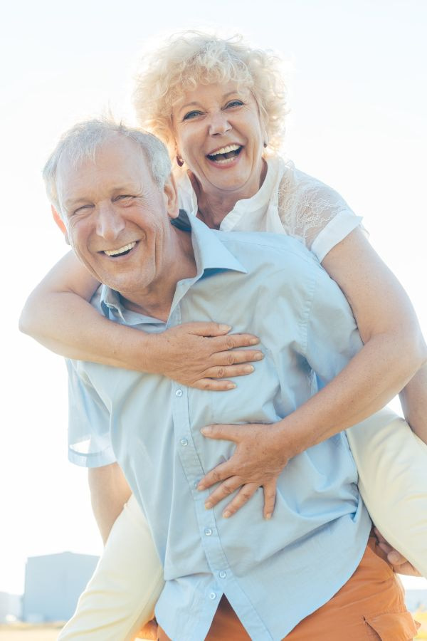 image of an older couple smiling while giving each other a 'piggy back ride'