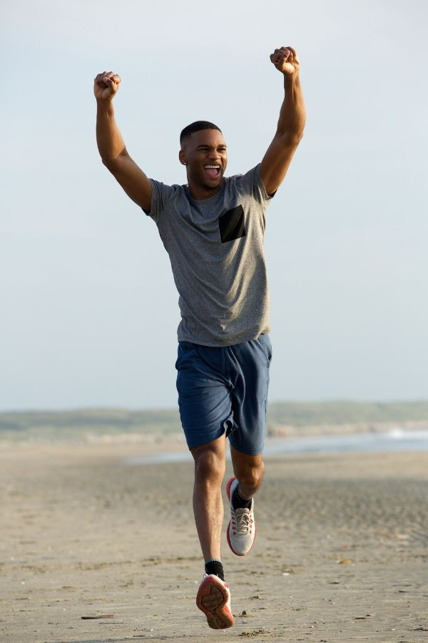 image of a man running down a beach with his arms raised triumphantly